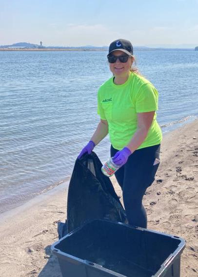 Woman in neon tshirt and purple gloves picking up trash on a beach